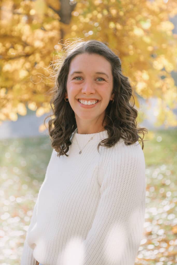 A photo of Libby Bloom, eating disorder dietitian in Durango, CO looking at the camera wearing a white sweater with yellow leaves in the background