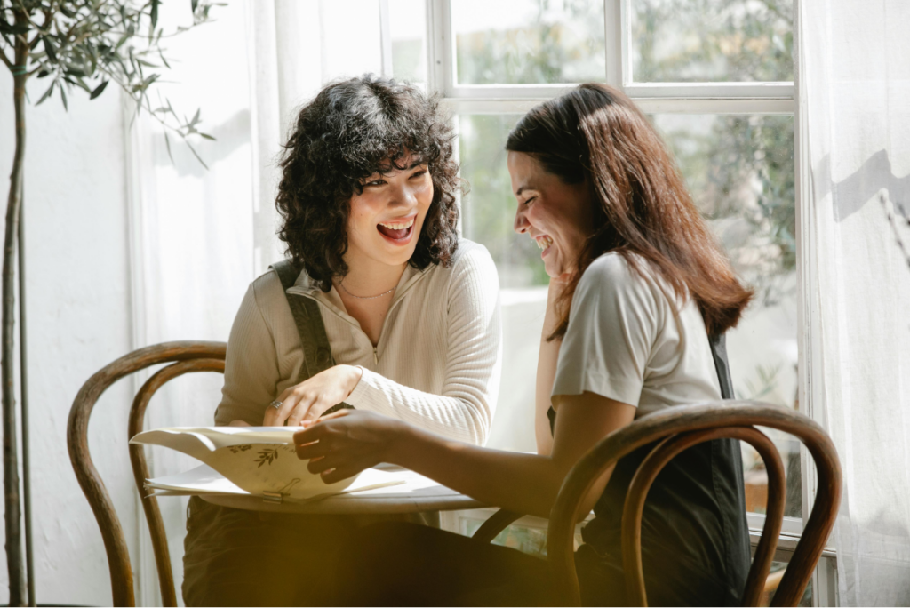 two women looking at a packet of paper. They are smiling and laughing